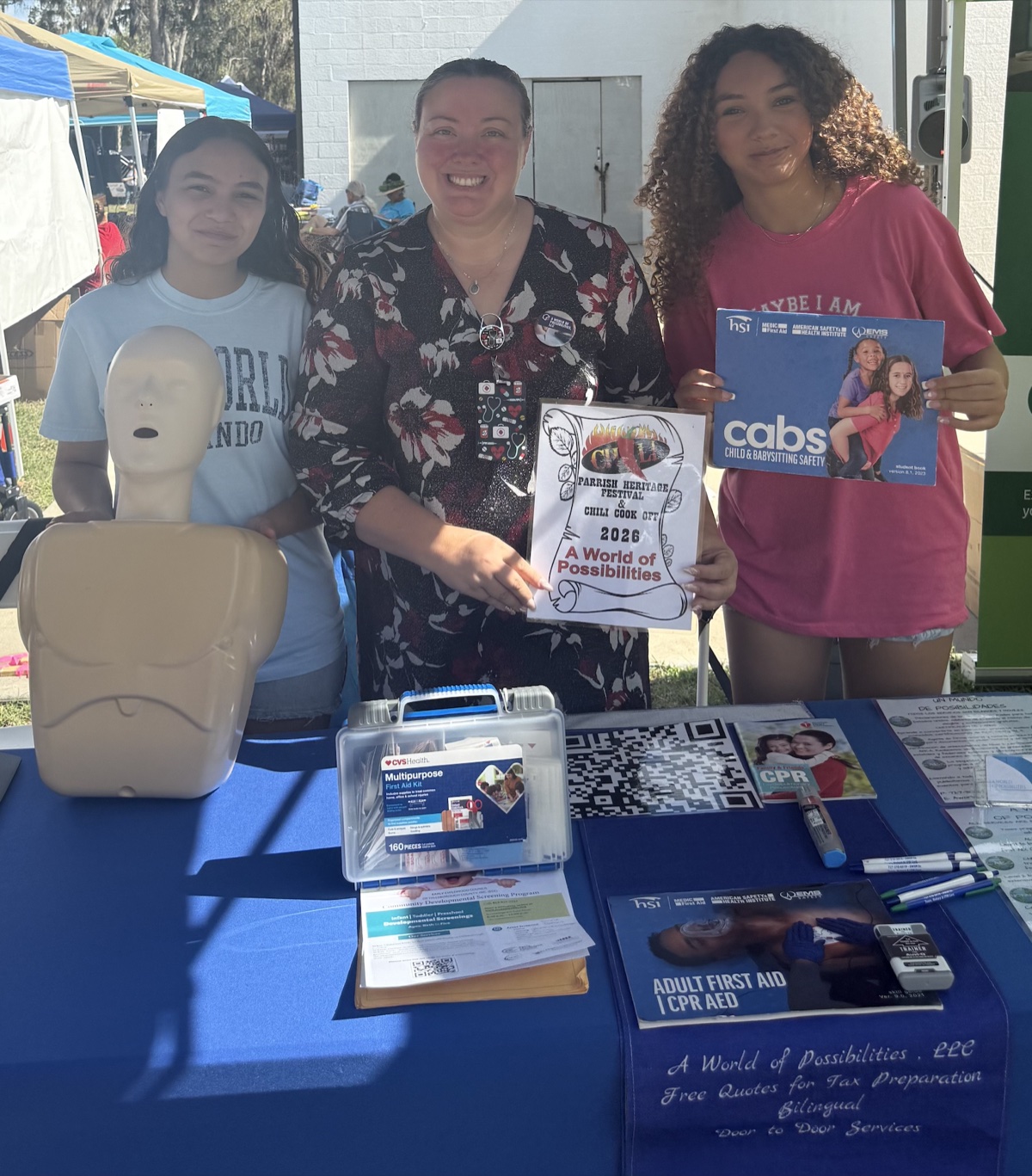 A World of Possibilities team at the Parrish Heritage Festival booth with CPR training manikin and CABS Child & Babysitting Safety materials
